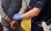 umundurowany policjant zakłada kajdanki zatrzymanemu mężczyźnie, który z rękoma z tyłu odwrócony jest do niego plecami