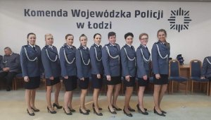 Zdjęcie jest zrobione podczas ślubowania w Komendzie Wojewódzkiej Policji. Widać na nim 9 policjantek w mundurach galowych. Mają na sobie szare marynarki, sznury galowe, pod spodem białe koszule i czarne spódniczki przed kolana. Wszystkie są zawodniczkami w reprezentacji policji polskiej piłki nożnej kobiet.