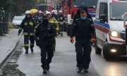 policjanci i strażacy idą drogą w tle wozy strażackie