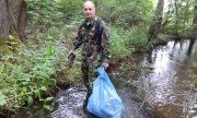Marcin Sikora stoi w strumyku i trzyma w ręce śmieci oraz worek ze śmieciami