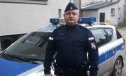 starszy sierżant Przemysław Romańczuk stoi przy radiowozie policyjnym
