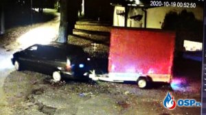ujęcie z kamery monitoringu w nocy , widać ciemny samochód kombi, który ciągnie przyczepę z czerwona plandeką