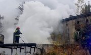 Strażak gasi pożar stojąc na dachu przy pomocy węża gaśniczego