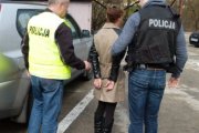 dwaj policjanci w kamizelkach z napisem Policja prowadzą zatrzymaną