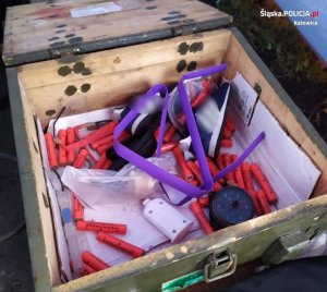 zdjęcie kolorowe: drewniana skrzynia w której włożone są materiały pirotechniczne, lont i buty sportowe w kolorze granatowym