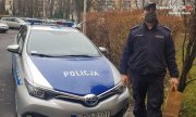 Dzielnicowy z Komisariatu II Policji w Bielsku-Białej idzie obok radiowozu podczas doręczania zakupów seniorce na kwarantannie