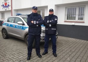 dwaj policjanci w mundurach stoją przed radiowozem