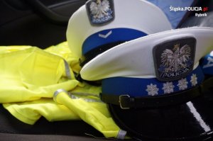 dwie policyjne czapki z białym otokiem leżące na żółtych kamizelkach