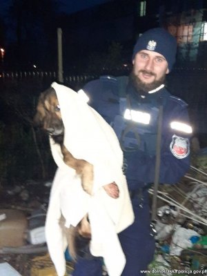 Na zdjęciu policjant trzyma na rękach zawiniętego w kocyk psa