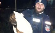 Na zdjęciu policjant trzyma na rękach zawiniętego w kocyk psa.&quot;&gt;