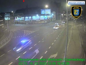 Zdjęcie z kamer monitoringu obrazujące skrzyżowania ulic Moniuszki Czarnieckiego w Legnicy. Na którym porusza się radiowóz oznakowany z włączonymi sygnałami świetlnymi oraz pojazd typu taxi