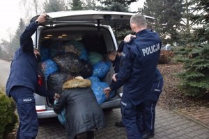 policjanci i pracownica cywilna wypakowują z bagażnika samochodu worki z plastikowymi nakrętkami