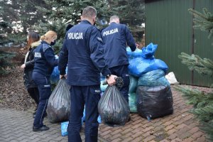 policjanci i pracownica cywilna składują worki z plastikowymi nakrętkami w wyznaczonym miejscu na terenie hospicjum