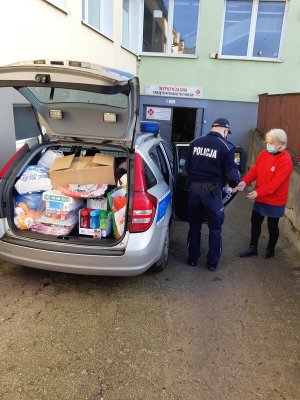 Policjant przekazuje zebrane produkty przez funkcjonariuszy przedstawicielce Caritasu