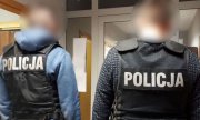 dwaj policjanci kryminalni w kamizelkach z napisem Policja stoją przed drzwiami
