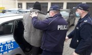 dwaj policjanci z zatrzymanym mężczyzną obok radiowozu policyjnego