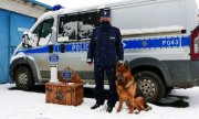 policjant i pies stoją obok skrzyni, na której stoi trofeum, za nimi stoi radiowóz