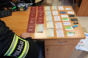 Policjant spisuje karty i dowody rejestracyjne od pojazdów i kart bankomatowe leżące na biurku