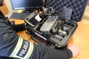 Policjant przegląda zawartość czarnej walizki, w której znajduje się dron
