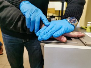 Technik kryminalistyki pobiera odciski palców od osoby zatrzymanej  na skanerze