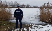 Umundurowany policjant stoi przed zamarzniętym zbiornikiem wodnym