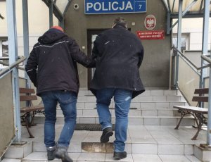 policjant prowadzi zatrzymanego po schodach do komendy policji