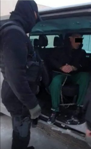 Zatrzymany skuty kajdankami siedzi w radiowozie, obok policjant