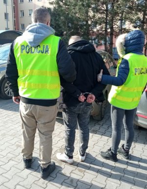 dwoje policjantów w kamizelkach odblaskowych z napisem policja prowadzą zatrzymanego