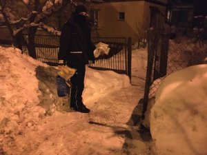 Policjant w ręku trzyma butelkę z wodą i opatrunki, w tle zaśnieżona posesja