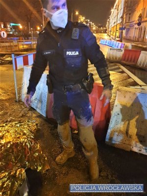 Zdjęcie przedstawia umundurowanego policjanta, który  spodnie i ręce ma całe w błocie