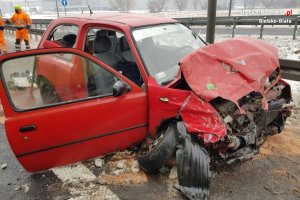 Czerwony samochód osobowy z rozbitym przodem stoi na pasie jezdni
