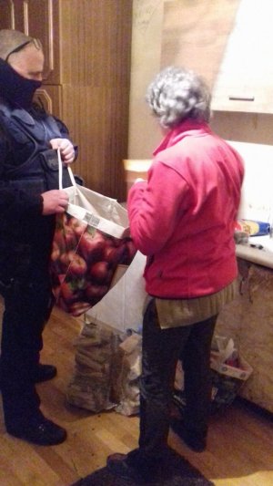 Seniorka wraz z umundurowanym policjantem, który przekazuje jej dary zebrane przez funkcjonariuszy - opał i jedzenie