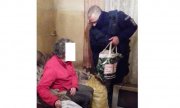 Na zdjęciu widoczny policjant przekazujący seniorce artykuły żywnościowe i opał zebrane przez funkcjonariuszy