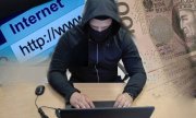 Zakapturzony i zamaskowany mężczyzna siedzący przy laptopie. W tle napis internet i banknot 100-złotowy