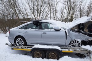 Na zdjęciu srebrny pojazd uszkodzony i zasypany śniegiem stojący na lawecie