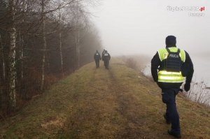 czterech umundurowanych policjantów idzie nasypem na skraju lasu - widok z tyłu