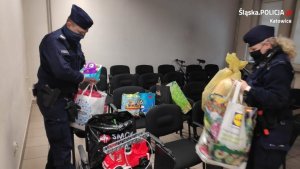 zdjęcie kolorowe: policjant i policjantka na sali odpraw pakują zabawki w foliowe torby