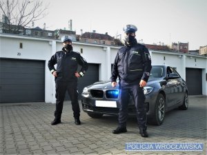 dwaj policjanci stoją obok radiowozu