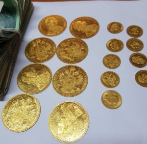 rozłożone złote monety, obok widoczny fragment pliku banknotów spiętych gumką