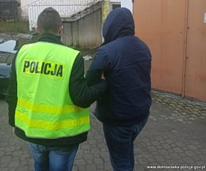 policjant w żółtej kamizelce z napisem Policja prowadzi osobę zatrzymaną