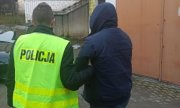 policjant w żółtej kamizelce z napisem Policja prowadzi osobę zatrzymaną