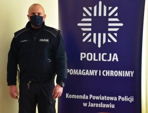 Policjant stojący obok baneru z napisem Policja Pomagamy i Chronimy Komenda Powiatowa Policji w Jarosławiu