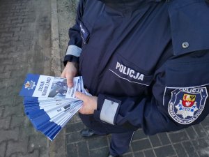 Policjant trzyma w dłoniach ulotki promujące zawód policjanta