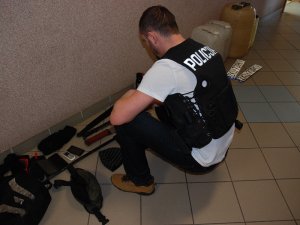 policjant ogląda zabezpieczone przedmioty leżące pod ścianą na podłodze