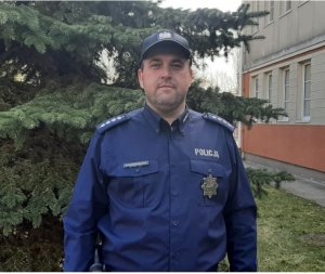 asp. szt. Paweł Kaźmierczak w mundurze. W tle budynek oraz drzewo
