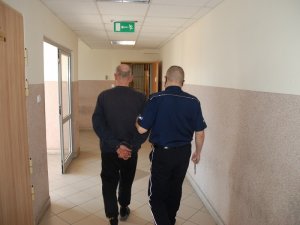 umundurowany policjant prowadzi korytarzem zatrzymanego mężczyznę