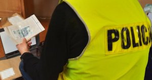 Mężczyzna w kamizelce z napisem policja trzyma w woreczku banknot