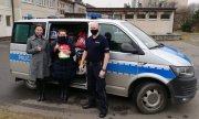 policjant umundurowany stoi przy radiowozie z dwiema kobietami, którym przekazuje prezenty dla dzieci