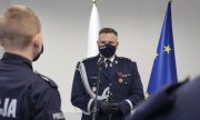mężczyzna w mundurze stoi przed mikrofonem, z tyłu widoczne są fragmenty flag