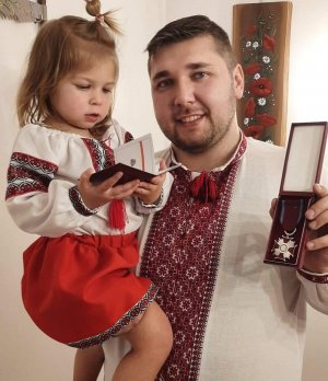 Zdjęcie przedstawia Piotra Ostaszewskiego z córeczką, trzymającym odznaczenie